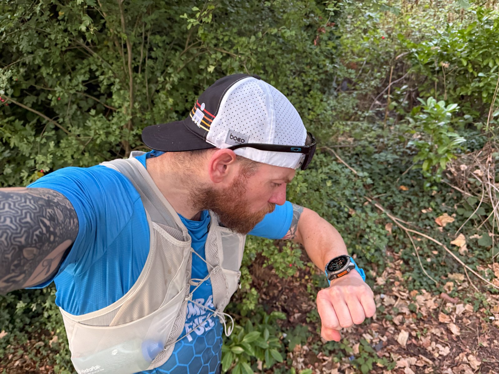 A relaxed runner on a countryside trail glancing at their watch while running at an easy, comfortable effort.