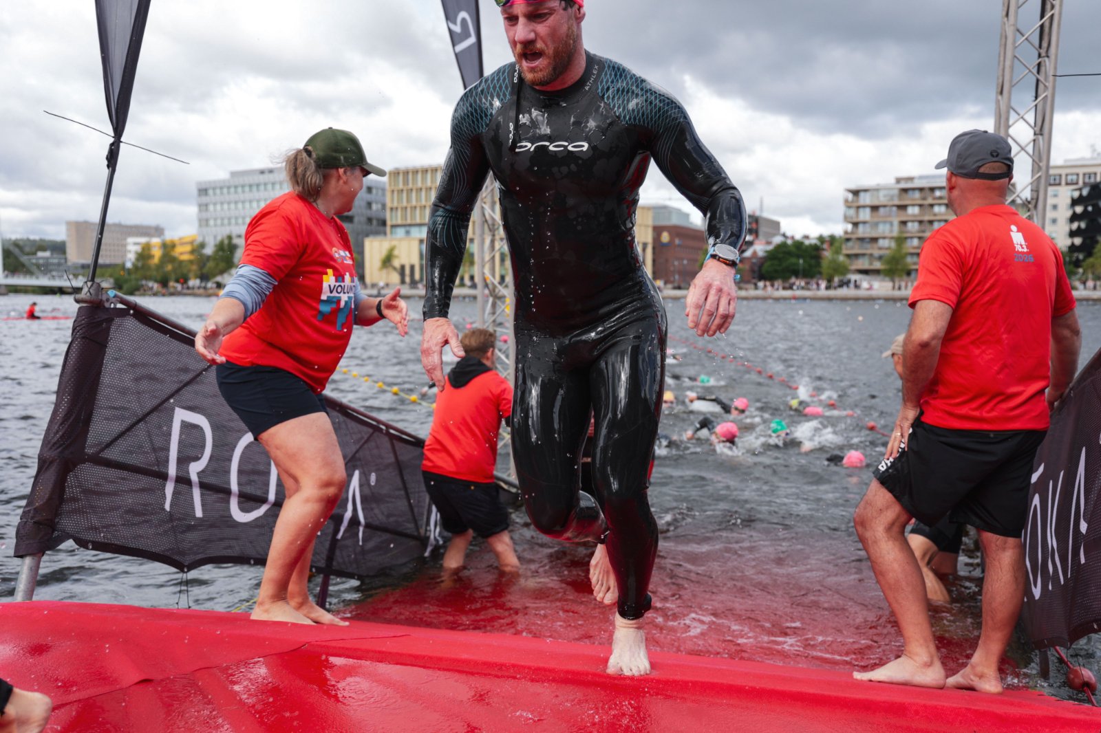A triathlete in a wetsuit exiting open water at dawn looking composed rather than exhausted.